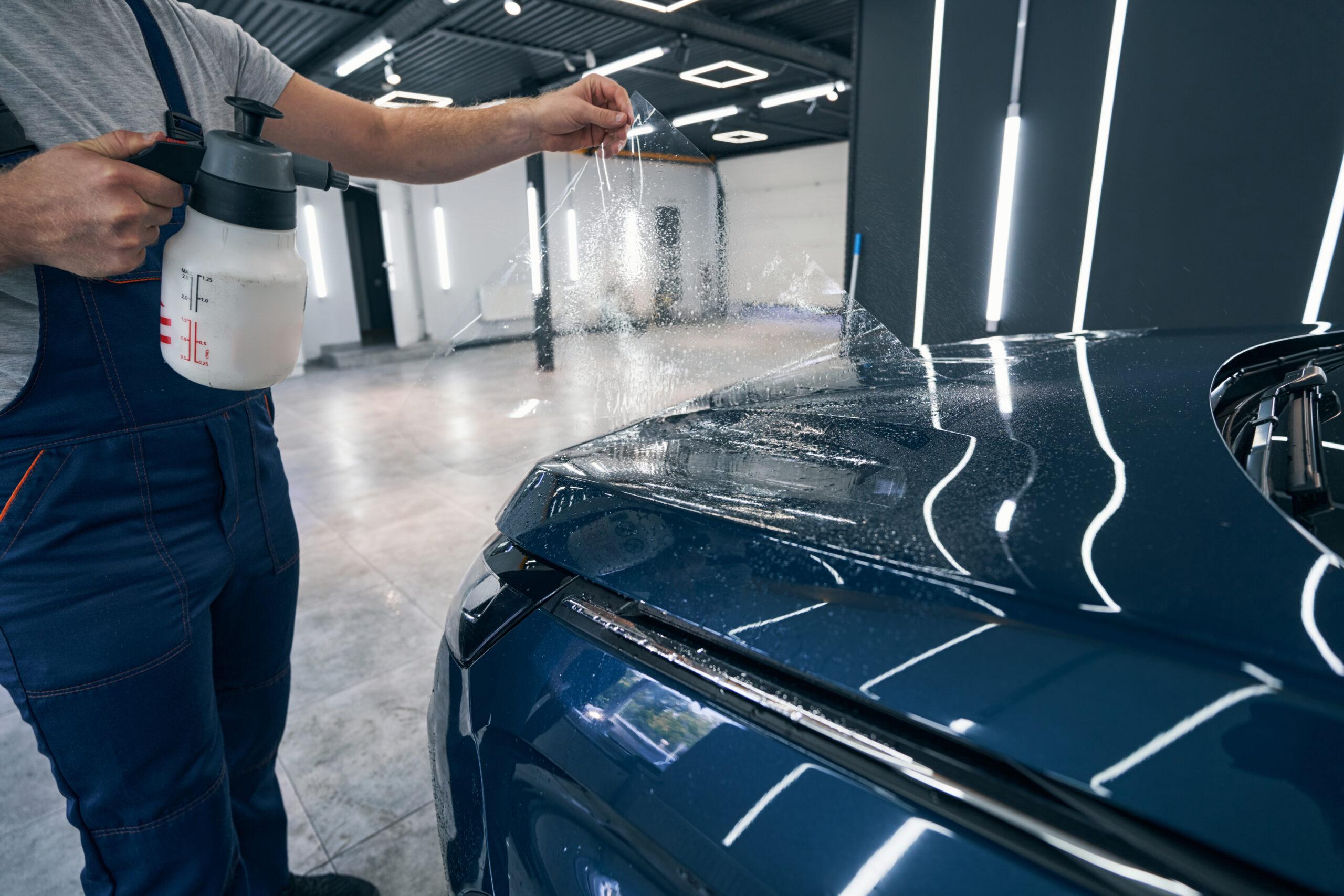 Auto wrapping specialist puts wet vinyl foil on car hood closeup