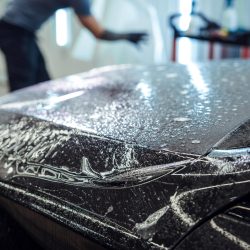 Sticker of a protective film on the headlight of a car in a car detailing studio. Man wrapping white car with polyurethane tape